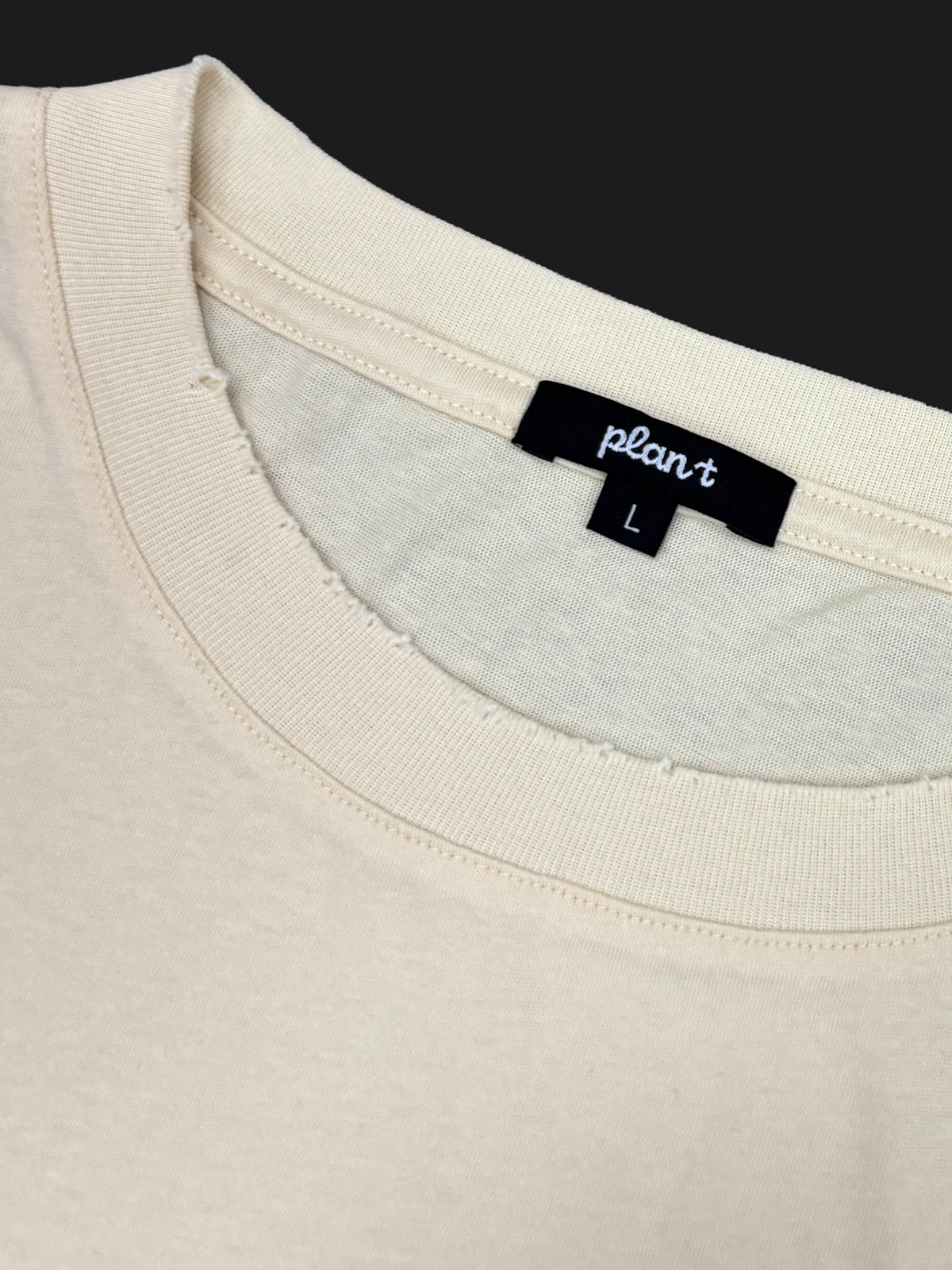 Close-up of a cream-colored t-shirt showing the inner neck label which reads 'plan t' and 'L'.
